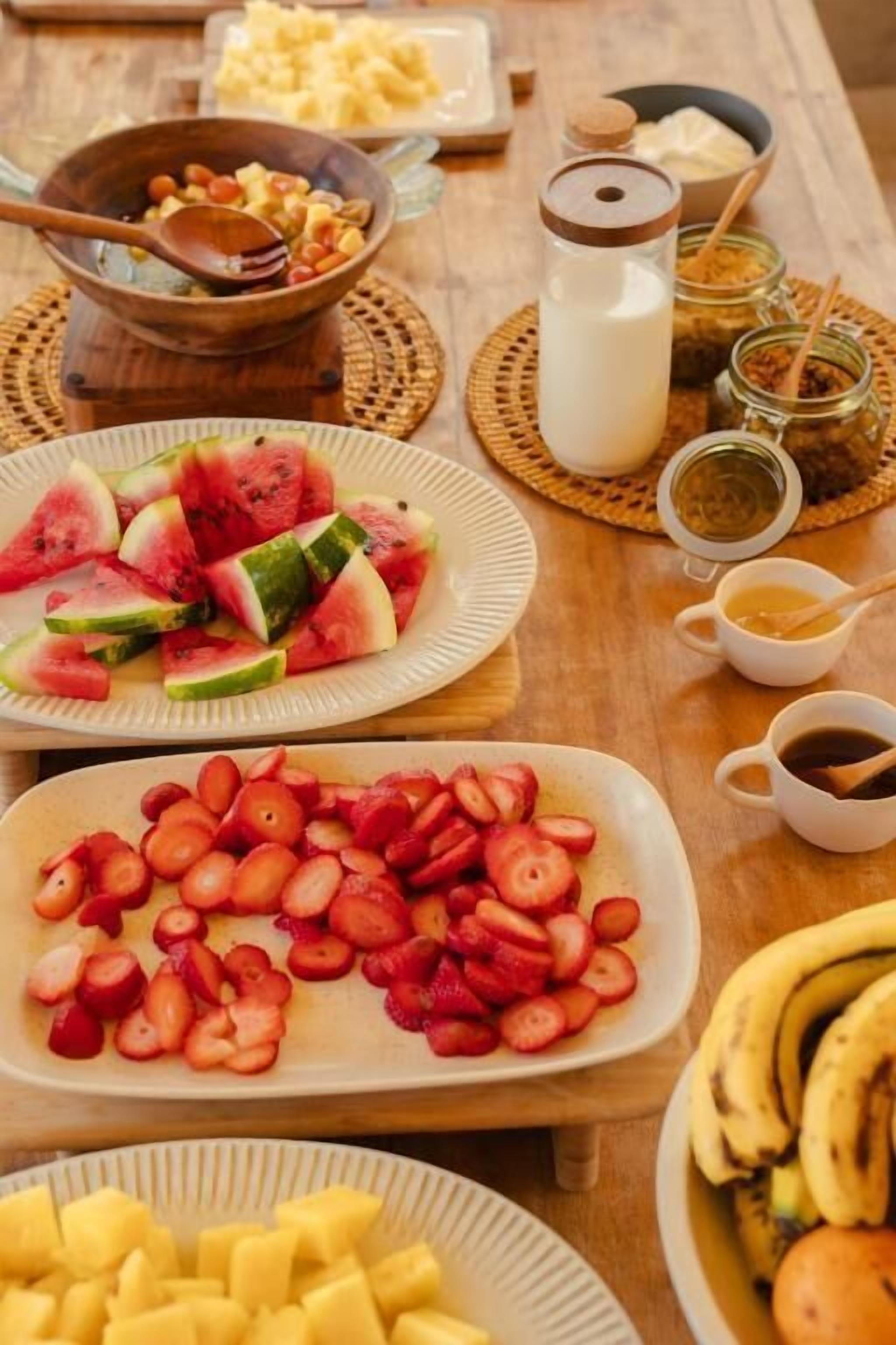 Ein Frühstückstisch mit Obstscheiben, einer Schüssel Müsli, einer Milchflasche und einer Tasse Kaffee.