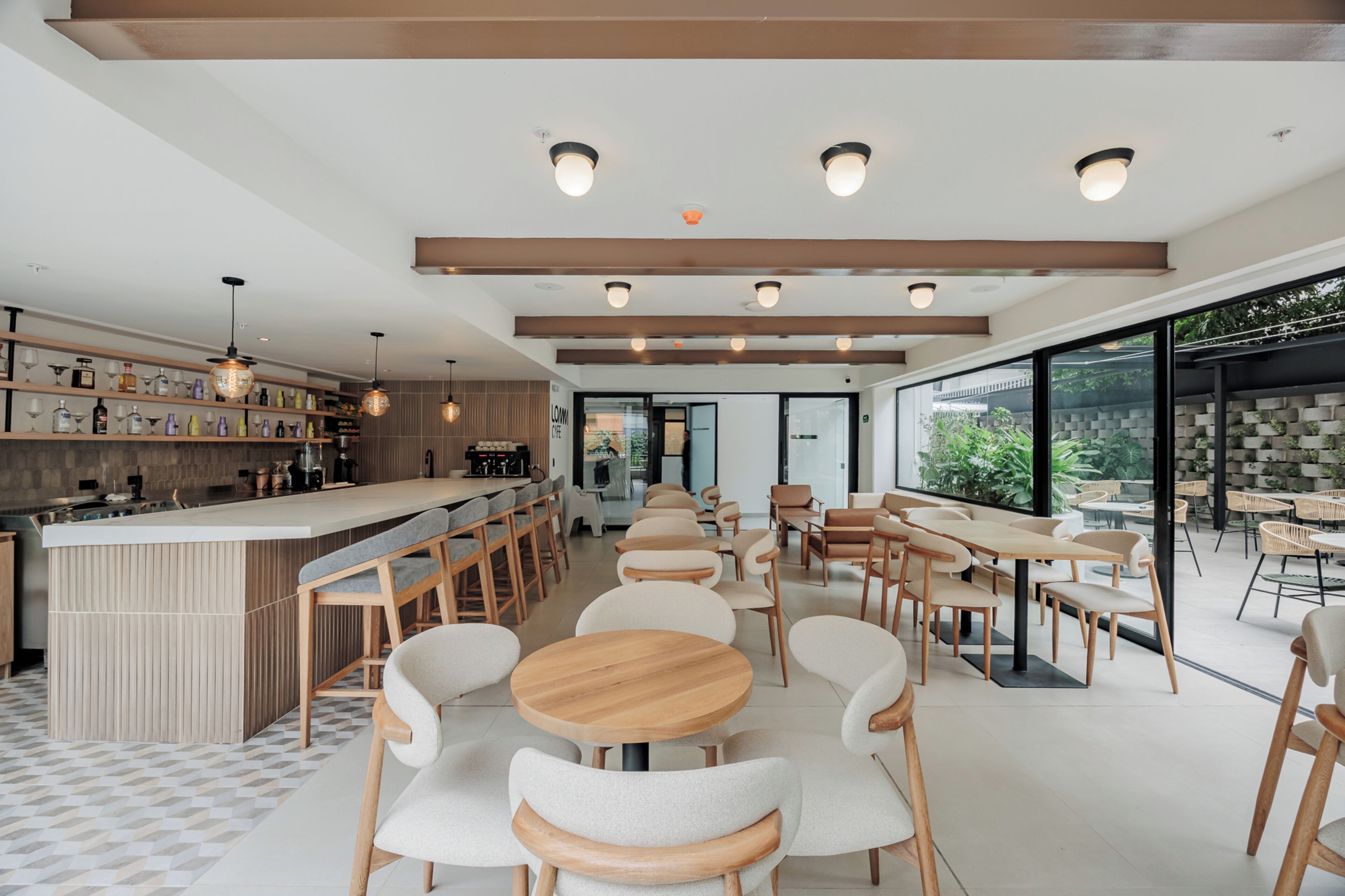 Een modern café met een bar, houten tafels en stoelen, en grote ramen met uitzicht op groen.