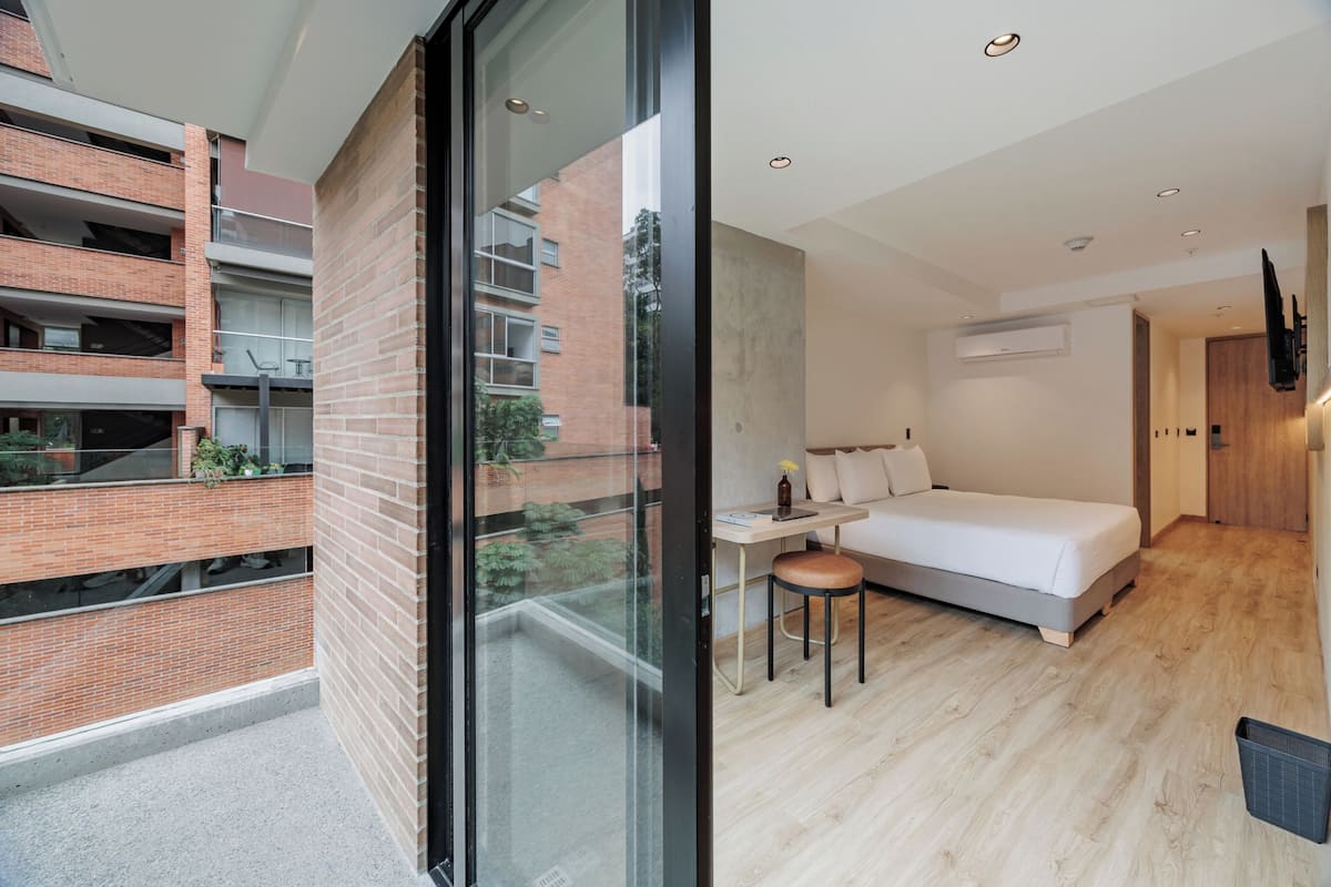 A modern apartment with a balcony, a bed, a desk, and a TV.