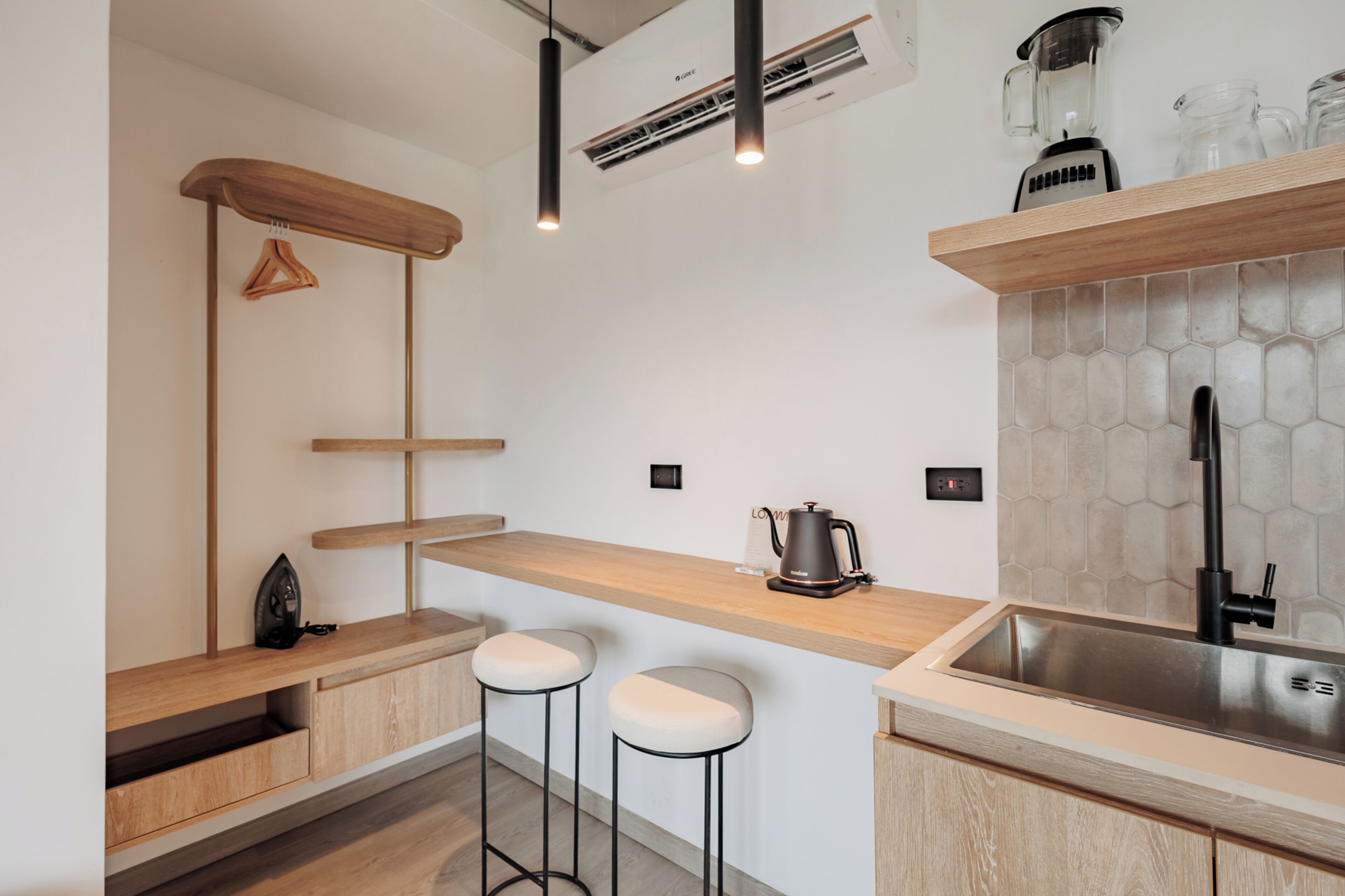 A modern kitchen with a wooden countertop, bar stools, a coffee machine, a sink, and an air conditioning unit.