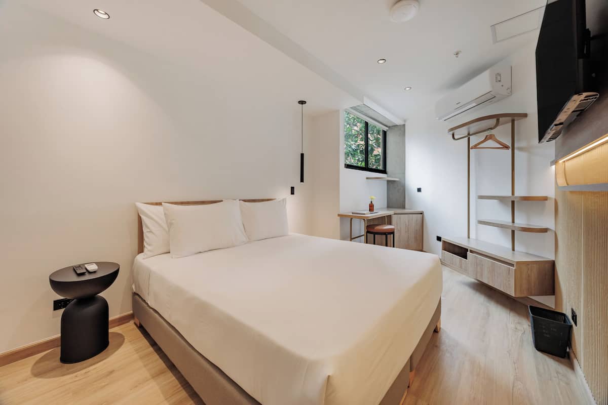 A modern hotel room with a large bed, a small desk, a chair, and a TV mounted on the wall.