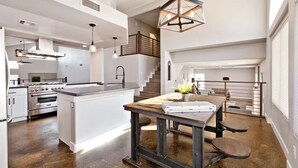 Een moderne keuken met een centraal eiland, roestvrijstalen apparatuur en een eethoek met een houten tafel en bank.
