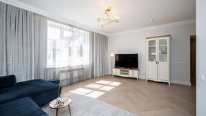 A modern living room with a dark blue sofa, a flat-screen TV, a cabinet, and a large window with sheer curtains. - Toompea Castle 2 BR Old Town Apartment (Tallinn)