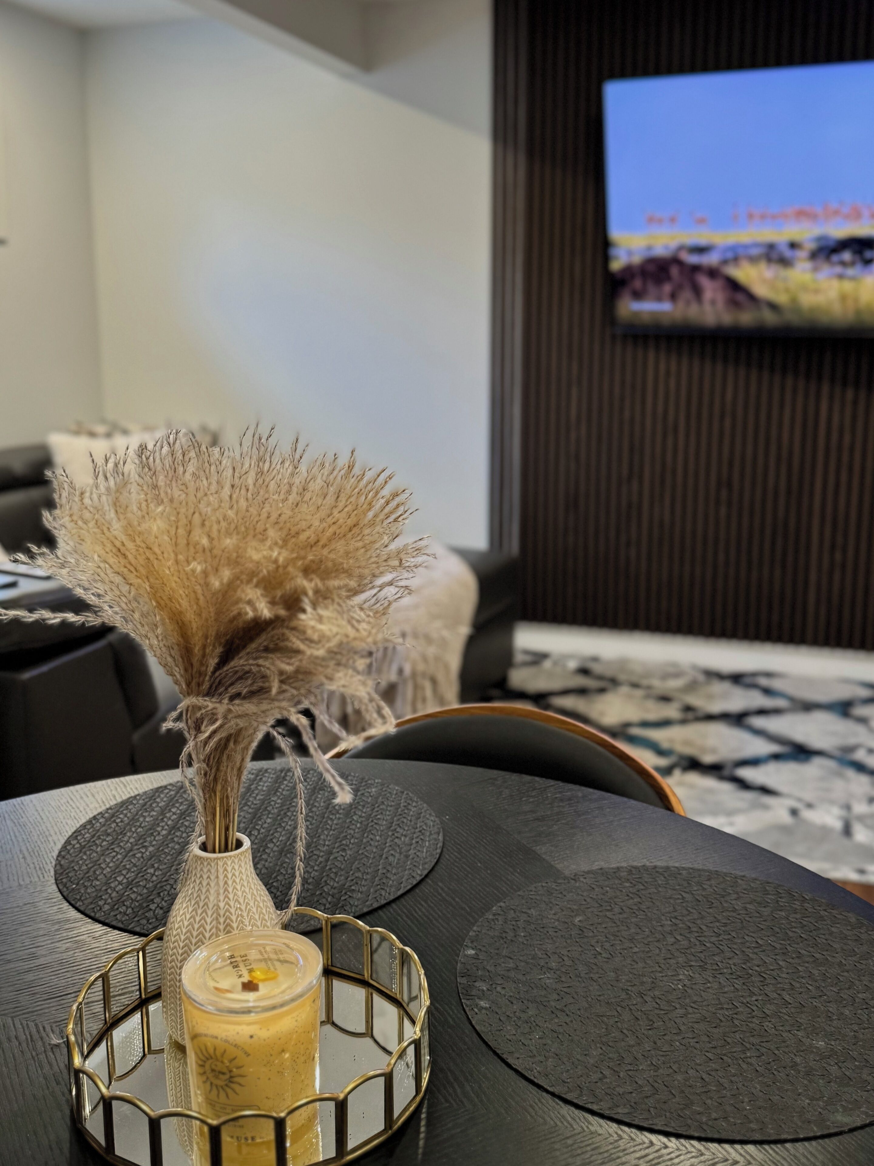 Una sala moderna con un jarrón decorativo sobre una mesa negra, un sofá y un televisor montado en la pared.