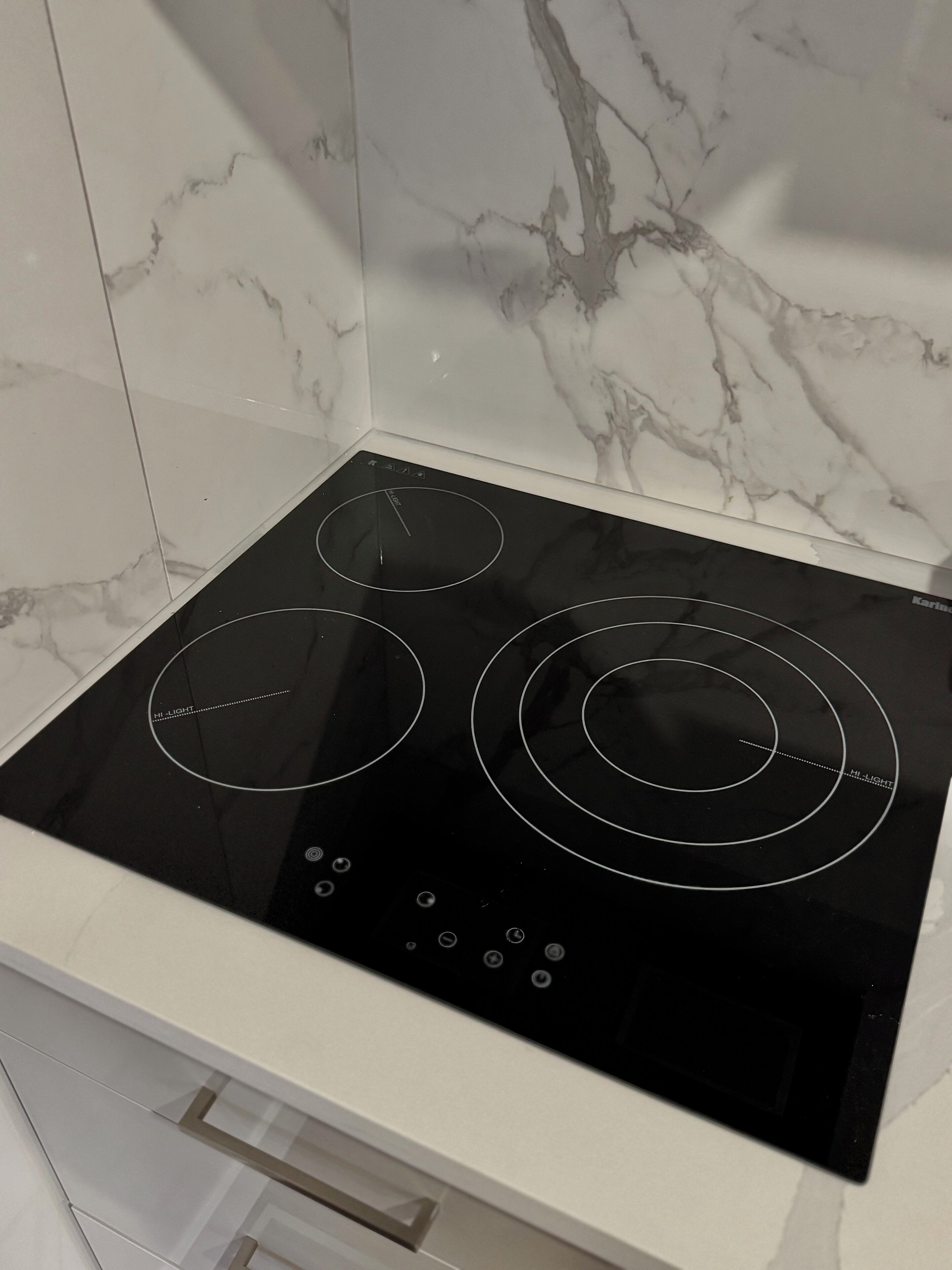 Une plaque de cuisson à induction noire, dotée de trois boutons de commande et d’un écran numérique, le tout installé sur un fond de crédence en marbre blanc.