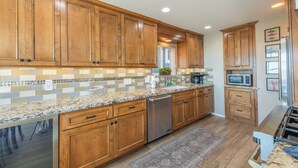 A kitchen with wooden cabinets, granite countertops, stainless steel appliances, and a tiled backsplash. - Beach Bum Retreat (Cayucos)