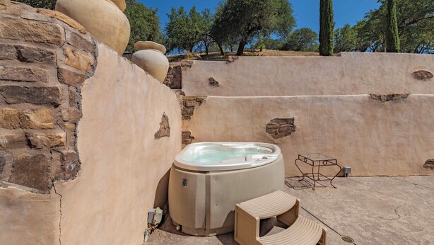 Un bain à remous dans un espace extérieur entouré de murs en pierre, avec une petite table et un banc.