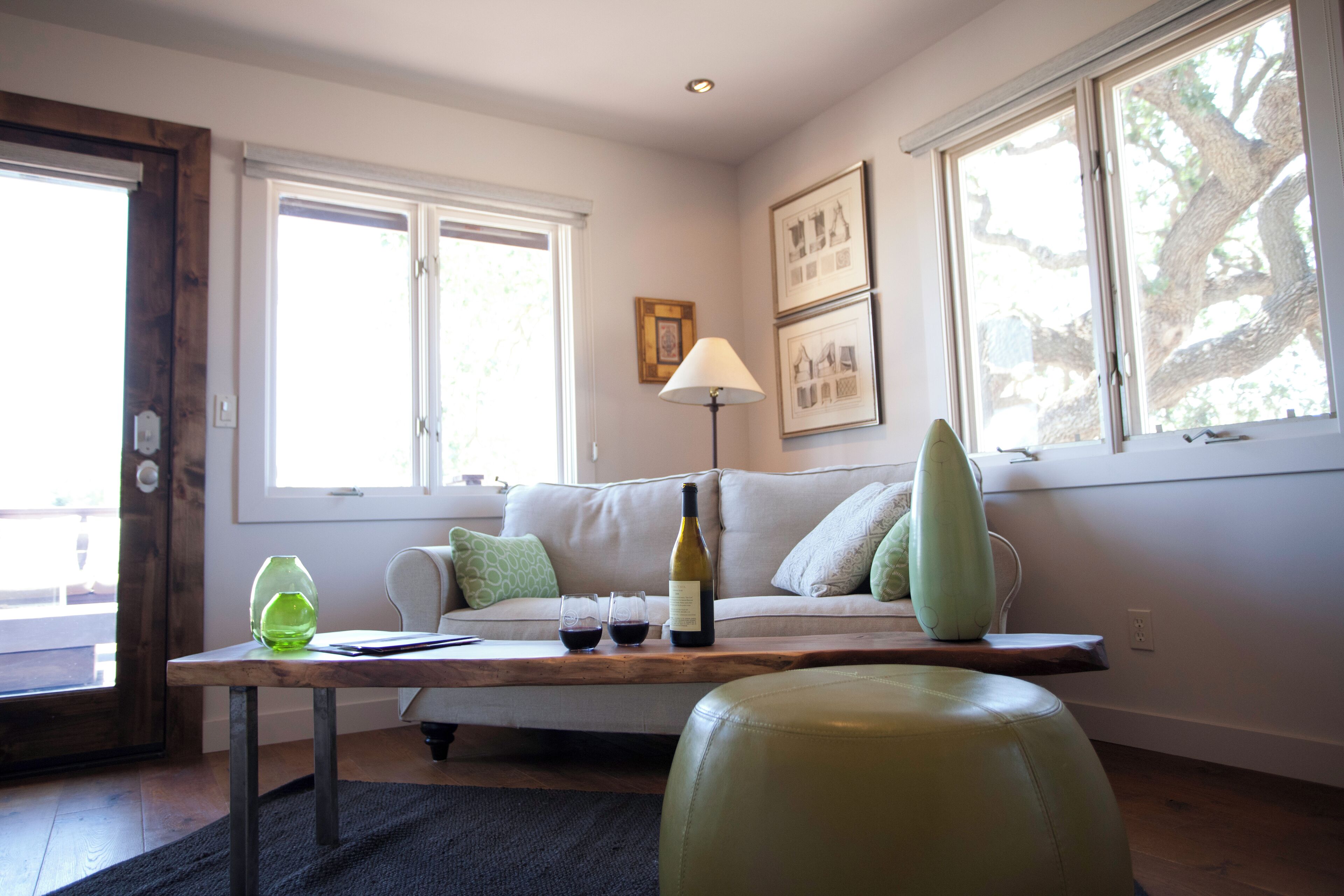 Una sala de estar con sofá, mesa de centro, lámpara y ventana con vista a árboles.