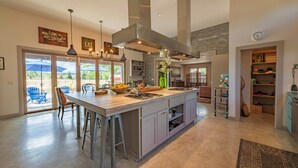 A spacious kitchen with a large island, bar stools, and a view through the glass doors. - Refugio Cosetta (Paso Robles)