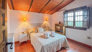 A bedroom with a bed, two bedside tables, a nightstand, a shelf with towels, and a window with a view. - La Zaranda de Pinillos Antequera by Ruralidays (Málaga)