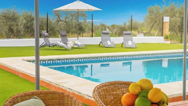 A poolside area with lounge chairs and a wicker basket with fruits. - La Zaranda de Pinillos Antequera by Ruralidays (Málaga)