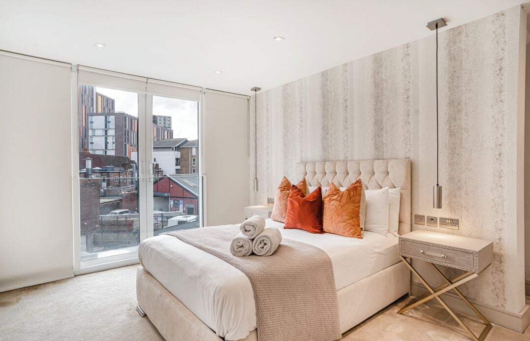 Un dormitorio moderno con una cama grande, vistas a edificios a través de ventanas de gran altura y una decoración minimalista.