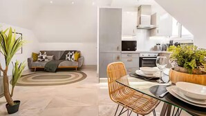 A modern living room with a sofa, a dining table with chairs, and a kitchen in the background.