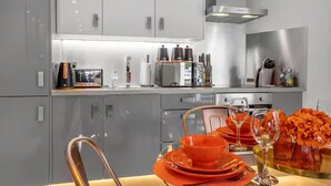 Una cocina moderna con armarios grises, electrodomésticos de acero inoxidable y un comedor con platos naranjas y un florero.