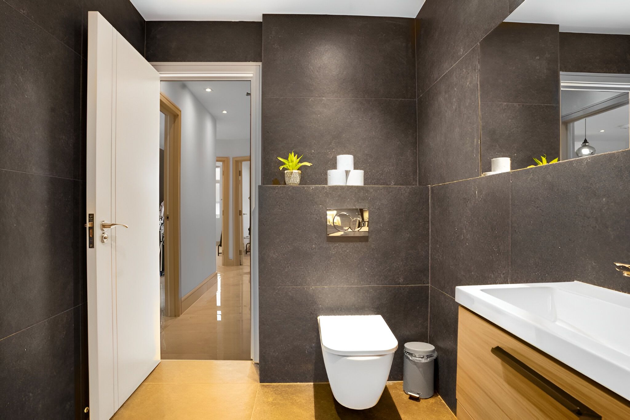 A modern bathroom with a large white bathtub, a toilet, and a sink. There is a mirror above the sink and a small potted plant on the wall.