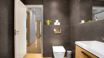 A modern bathroom with a large white bathtub, a toilet, and a sink. There is a mirror above the sink and a small potted plant on the wall.