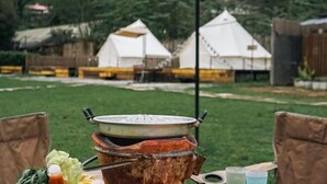 Un'accogliente area pranzo all'aperto con un'ampia pentola su un fornello a legna, circondata da sedie e un tavolo con verdure e bevande.