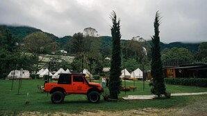 Un veicolo fuoristrada rosso parcheggiato in una zona erbosa con tende e alberi sullo sfondo.
