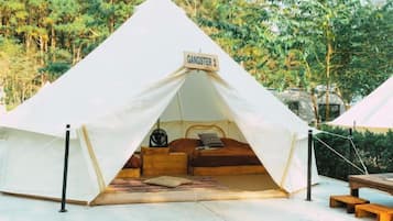 Una tenda con un cartello che recita 'GANGSTER 2' allestita in zona boschiva, con una panca di legno e un tavolo da picnic nelle vicinanze.