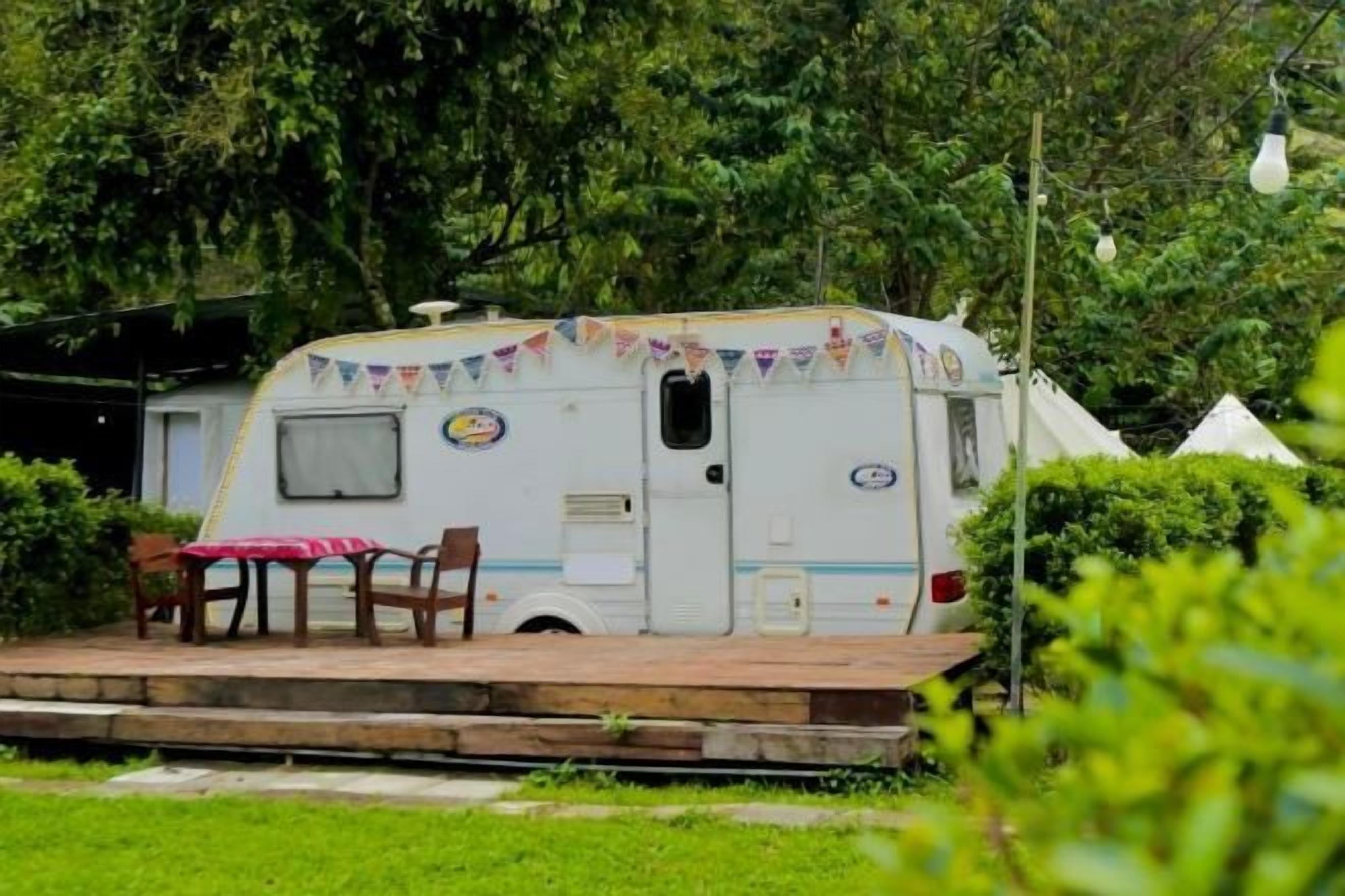 A white RV with a small porch area, a table, and chairs.
