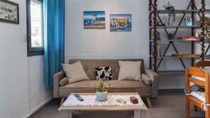 A living room with a sofa, a coffee table with a plant, a bookshelf, and two paintings on the wall. - Thena apartment IN the city center (Limenas Chersonisou)