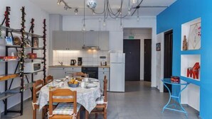 A modern kitchen with white cabinets, a dining table set for four, and a blue accent wall. - Thena apartment IN the city center (Limenas Chersonisou)