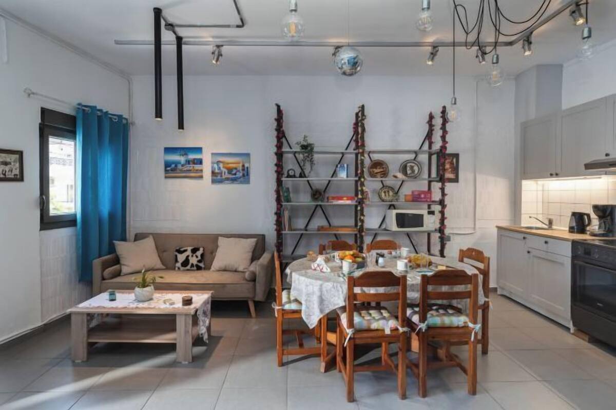 Ein modernes Wohnzimmer mit Sofa, Couchtisch, Esstisch mit Stühlen, einer Küchenzeile mit Schränken und Geräten sowie einer Wandregal mit Dekoration.