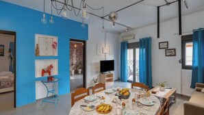 A modern living room with a dining area, blue walls, a TV, and a dining table set with plates and fruits. - Thena apartment IN the city center (Limenas Chersonisou)