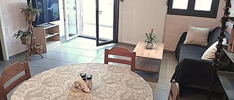 A living room with a round table, a sofa, a TV, and a sliding glass door leading to an outdoor area.