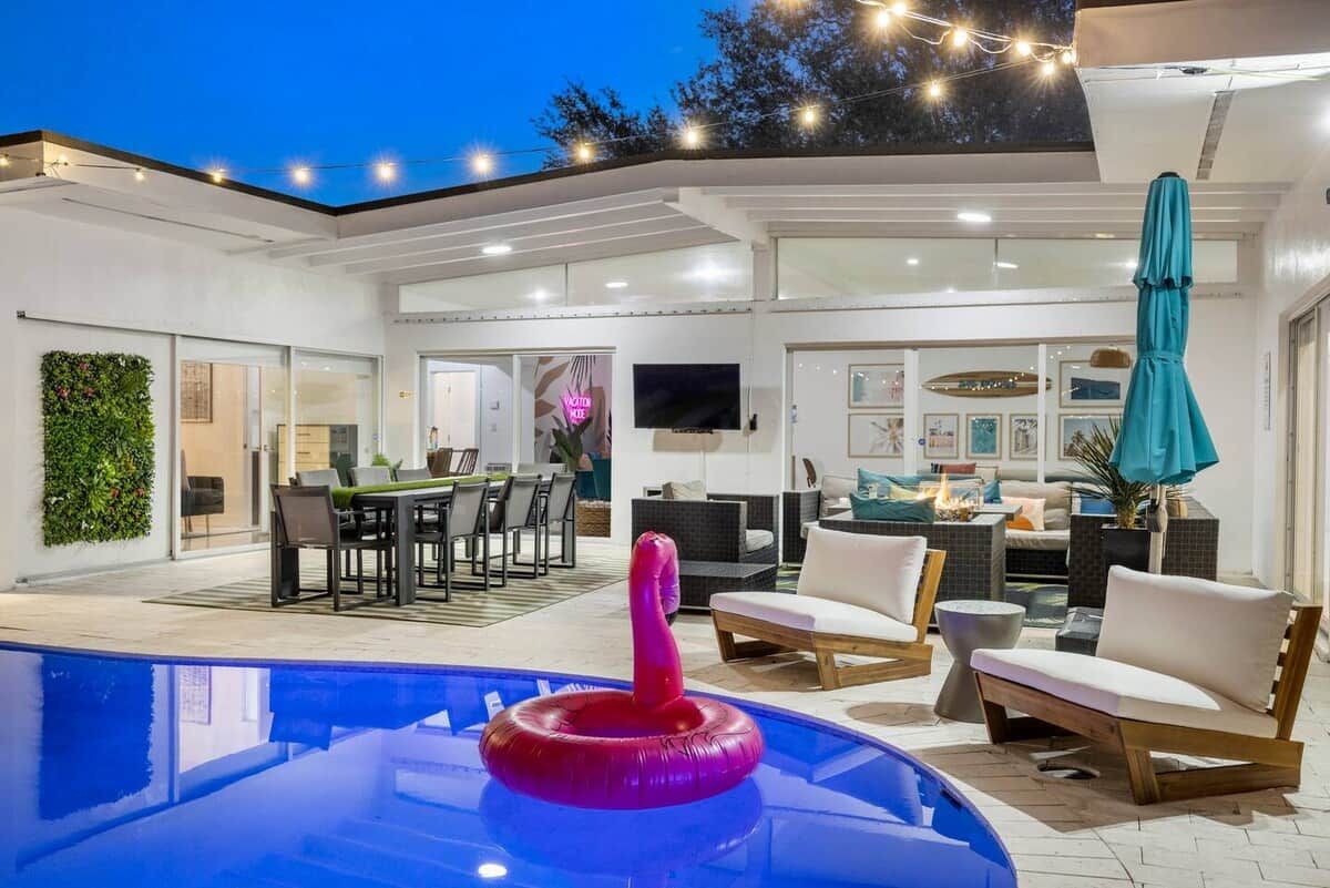 A modern outdoor pool area with a pink flamingo float, surrounded by outdoor furniture and a dining area.