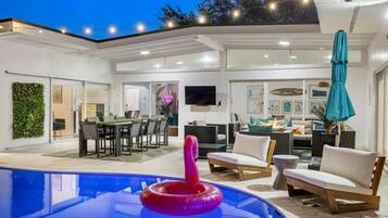A modern outdoor pool area with a pink flamingo float, surrounded by outdoor furniture and a dining area.