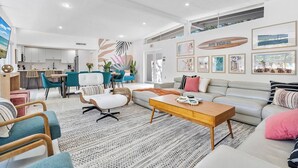 Un salon moderne avec un canapé, une table basse et des fauteuils. On y trouve également un coin repas avec une table et des chaises. La pièce est dotée d’une grande fenêtre et les murs sont ornés d’œuvres d’art.