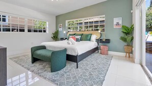 Une chambre moderne avec un lit, un fauteuil vert, une table de chevet et une fenêtre donnant sur un paysage verdoyant.
