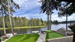 A lakeside property with a grassy lawn, a dock with boats, and a small shed. - Lakefront Retreat - Dock, Golf, Hot Tub & Arcade (Shelton)