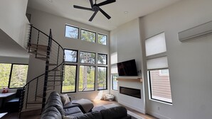 A spacious living area with a large window, a ceiling fan, and a staircase leading to an upper level. - Lakefront Retreat - Dock, Golf, Hot Tub & Arcade (Shelton)