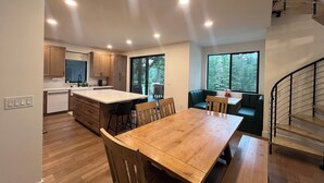 A modern kitchen with wooden cabinets, a large island, and a dining area with a wooden table and chairs. There is a staircase leading to an upper level. - Lakefront Retreat - Dock, Golf, Hot Tub & Arcade (Shelton)