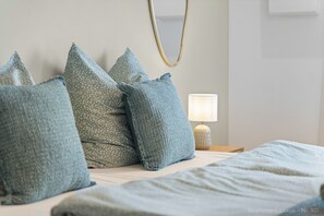 A neatly made bed with pillows, a bedside lamp, and a wall-mounted mirror.