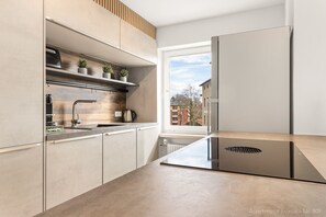 A modern kitchen with a built-in stove, a window with a view of buildings, and a shelf with plants. - Luxury suite with whirlpool in the center (Bad Aibling)