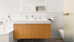 Ein modernes Badezimmer mit einem Holz-Waschtisch, einem weißen Waschbecken, einem Spiegel, einer Dusche und einer Toilette.