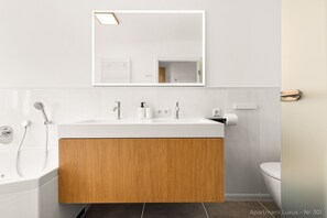 A modern bathroom with a wooden vanity, a white sink, a mirror, a shower, and a toilet. - Luxury suite with whirlpool in the center (Bad Aibling)