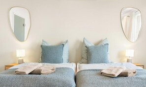 A hotel room with two beds, each with a pillow and a folded towel. There are bedside lamps and wall-mounted mirrors. - Luxury suite with whirlpool in the center (Bad Aibling)