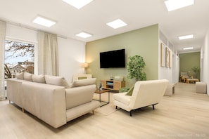 Una sala de estar moderna con sofá, sillón, televisión y una planta.