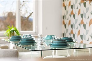 A dining table with glass top and blue plates, set in a modern apartment with geometric wallpaper and a view of trees outside. - Luxury suite with whirlpool in the center (Bad Aibling)