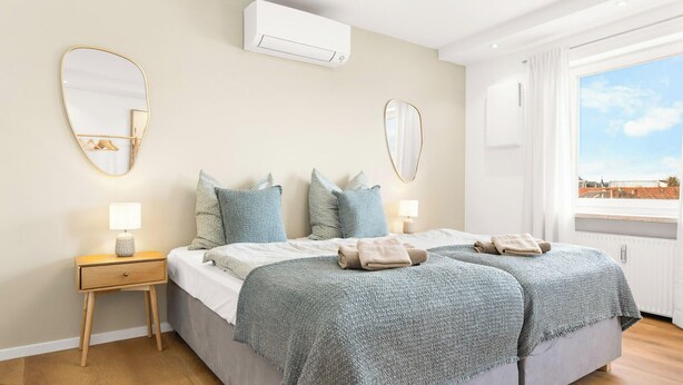 Ein Schlafzimmer mit Bett, Nachttischen, einem Spiegel und einer Klimaanlage.