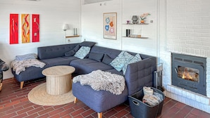 A modern living room with a sectional sofa, a round wooden coffee table, a fireplace, and a brick floor. - Nice home in Aabenraa with swimming pool (Aabenraa)