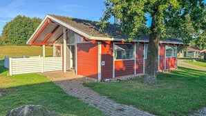 A red and white building with a sloped roof, a paved pathway leading to the entrance, and a grassy area with trees. - Nice home in Aabenraa with swimming pool (Aabenraa)
