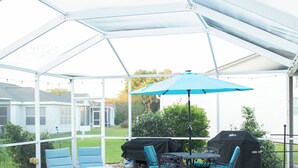 Ein überdachter Außenbereich mit Pool, Liegestühlen, einem Tisch mit Stühlen und einem Grill.