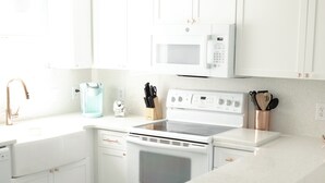 Eine moderne Küche mit weißen Schränken, einer Mikrowelle, einem Backofen und einer Kaffeemaschine.