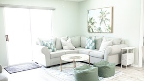 Ein modernes Wohnzimmer mit einem hellen Ecksofa, einem runden Couchtisch und grünen Sitzsäcken.