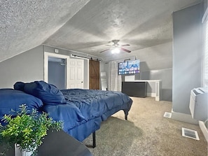 A bedroom with a bed, a ceiling fan, a television, and a radiator.